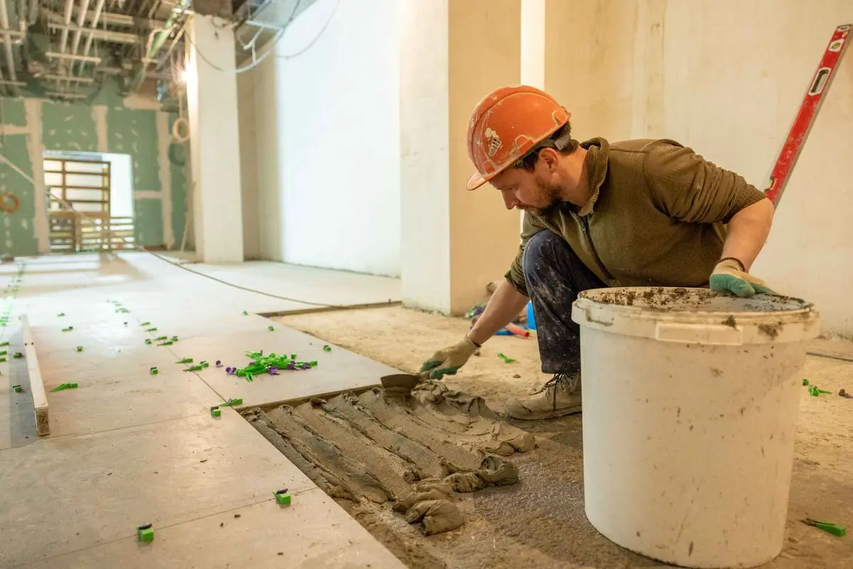 A tiler bedding floor tiles in a room being renovated