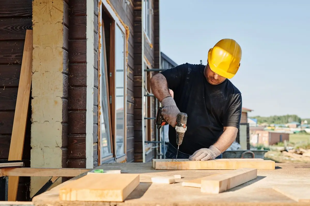A carpenter in a hard hat driving screws into a length of timber