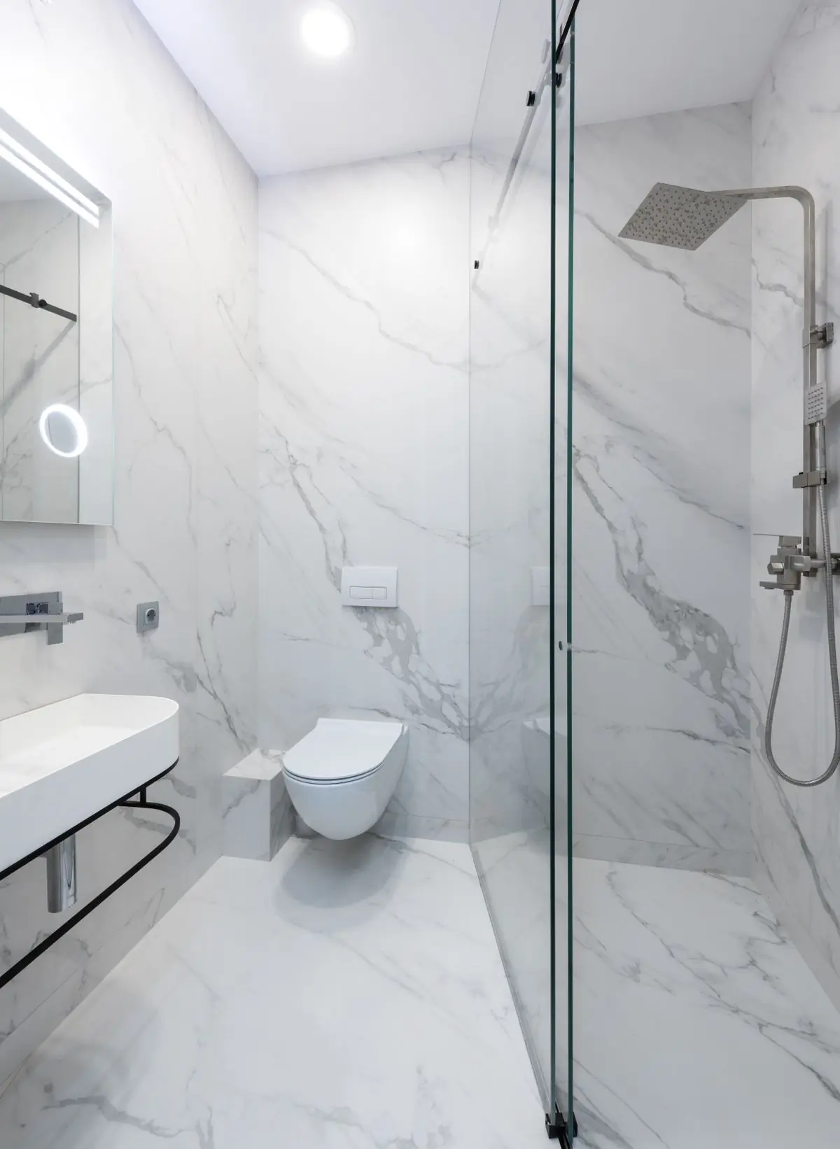 A finished bathroom with marble tiling and a glass screen