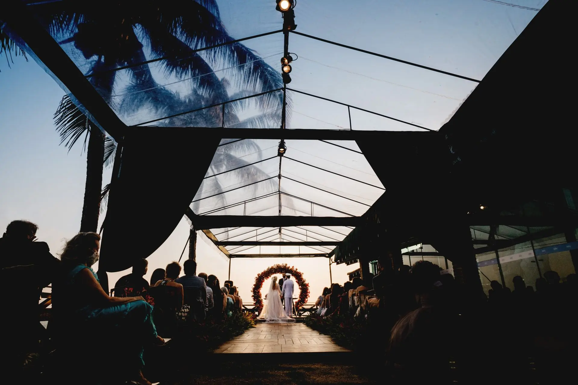 Guests standing as a bride walks the aisle under a marquee at sunset