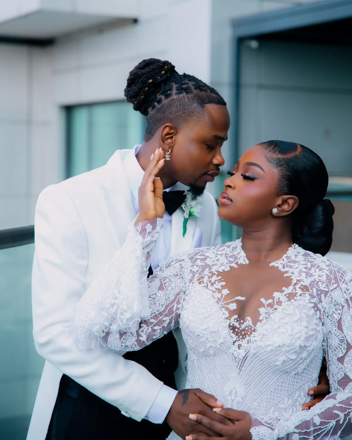 A couple in wedding clothes standing close together against a modern building
