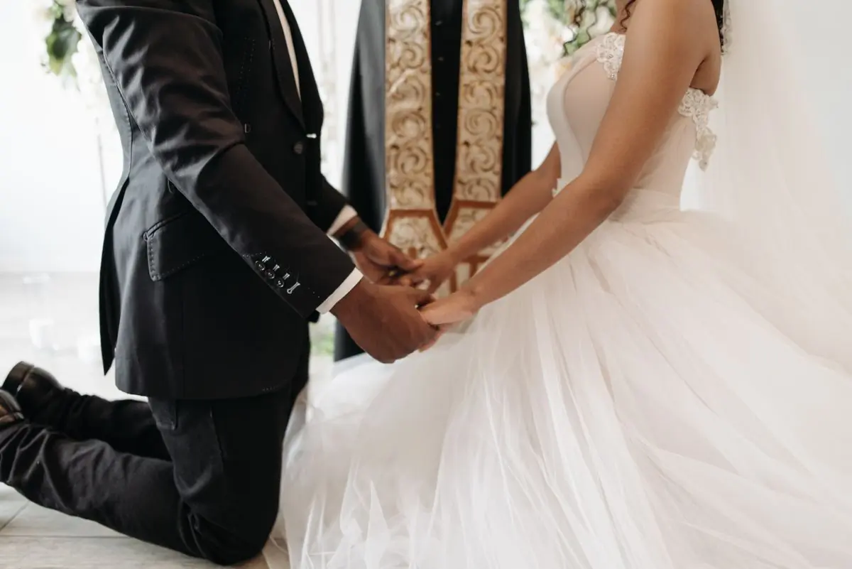 A groom kneeling to take his bride's hands during a ceremony