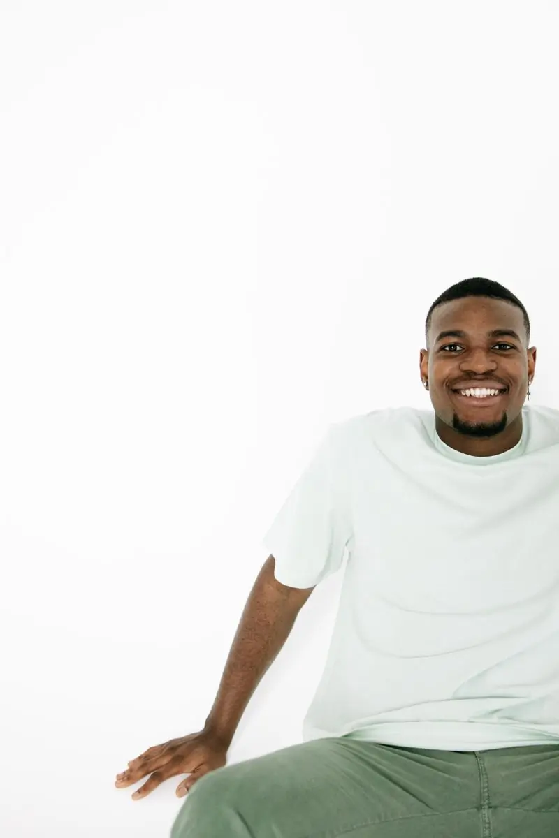 Kwame Sarpong seated and smiling against a white studio background