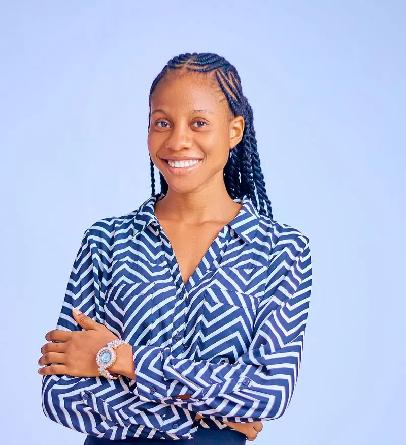Nana Ama Otoo in a patterned shirt, arms folded, against a pale blue background