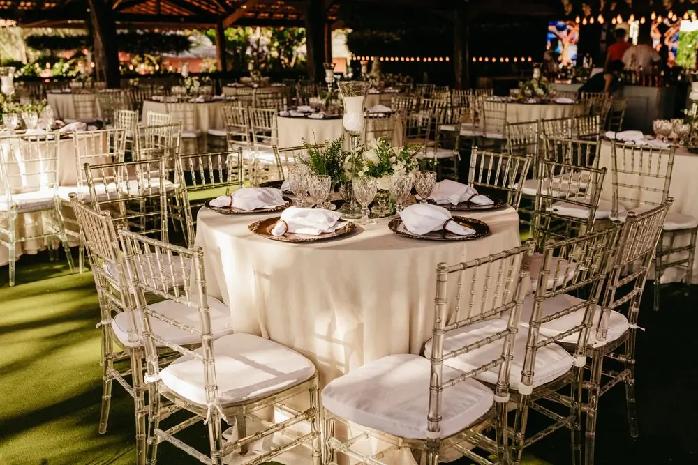 Tables and pale chairs laid out on a lawn at dusk before the guests arrive