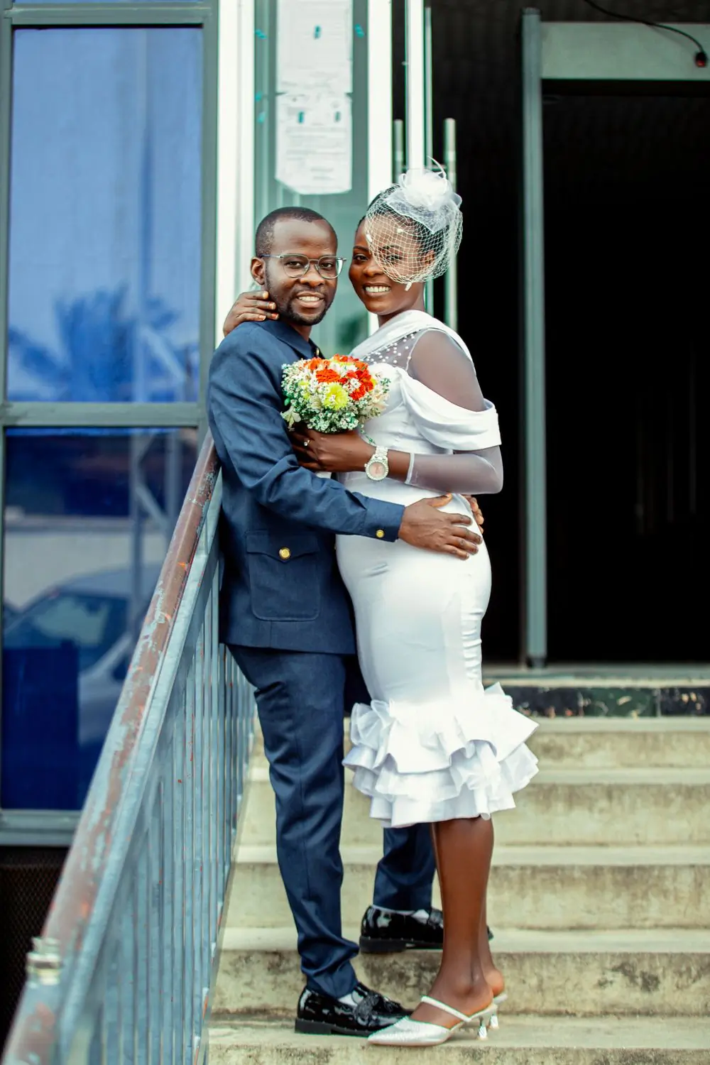 A couple in wedding clothes on an outdoor staircase, the bride holding her bouquet
