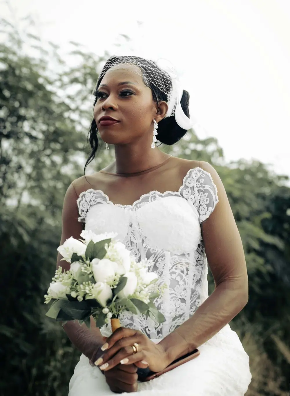 A bride in a white lace gown holding a bouquet of white roses