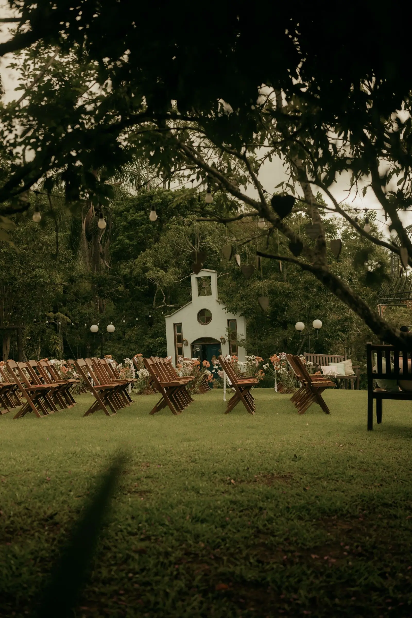 Rows of wooden chairs on a lawn in front of a small white chapel