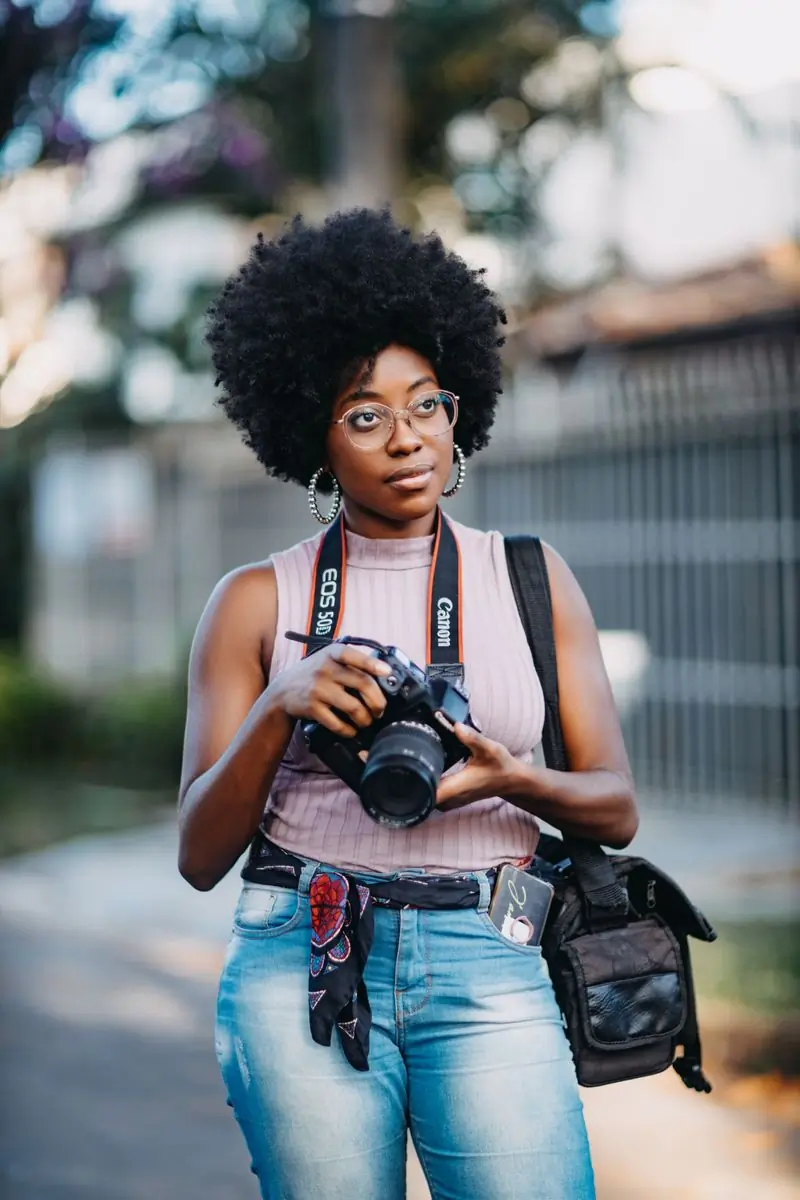 A photographer with a camera at her side, standing in the street