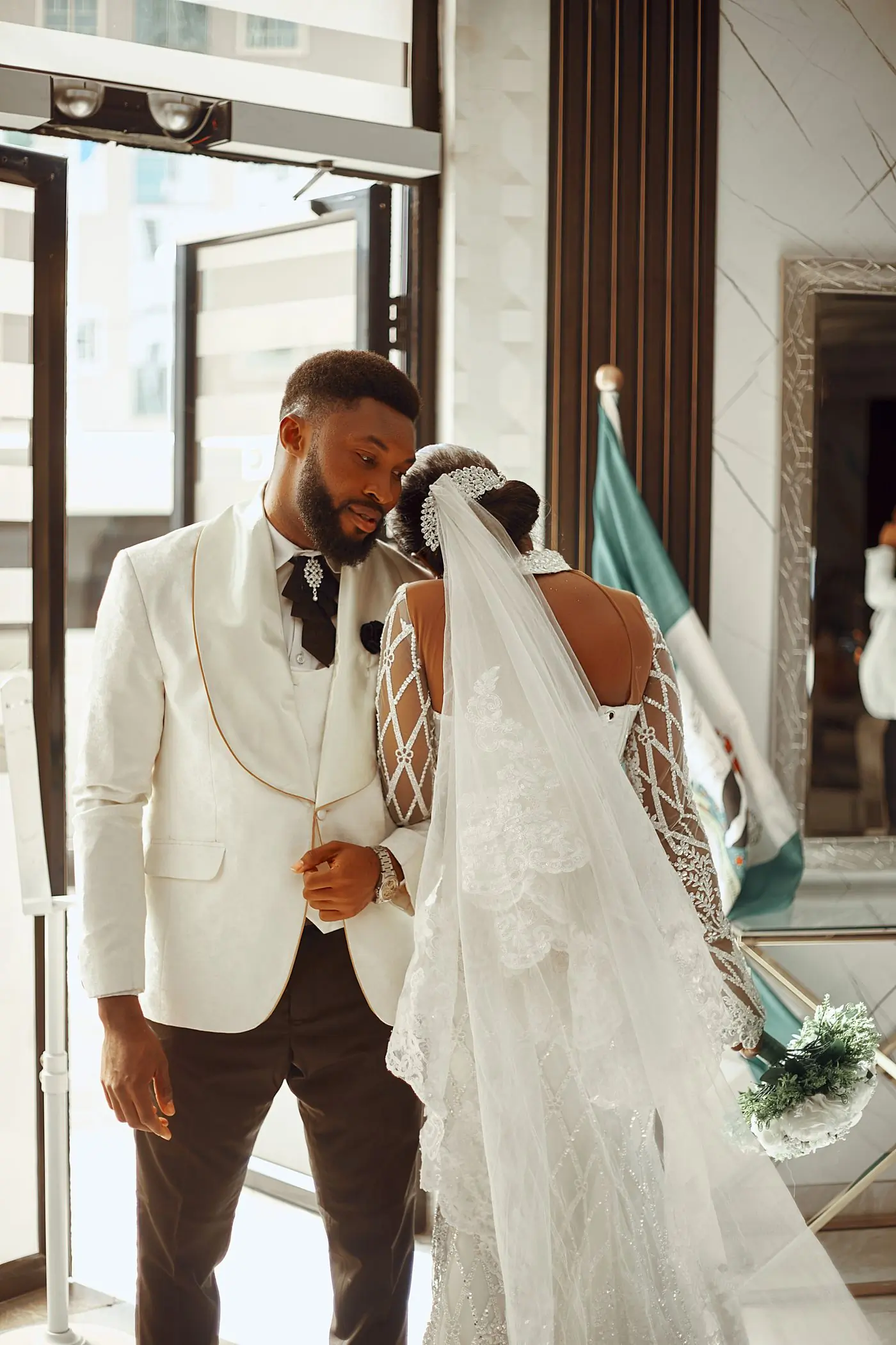 A groom in a white suit meeting his bride, her veil lifted