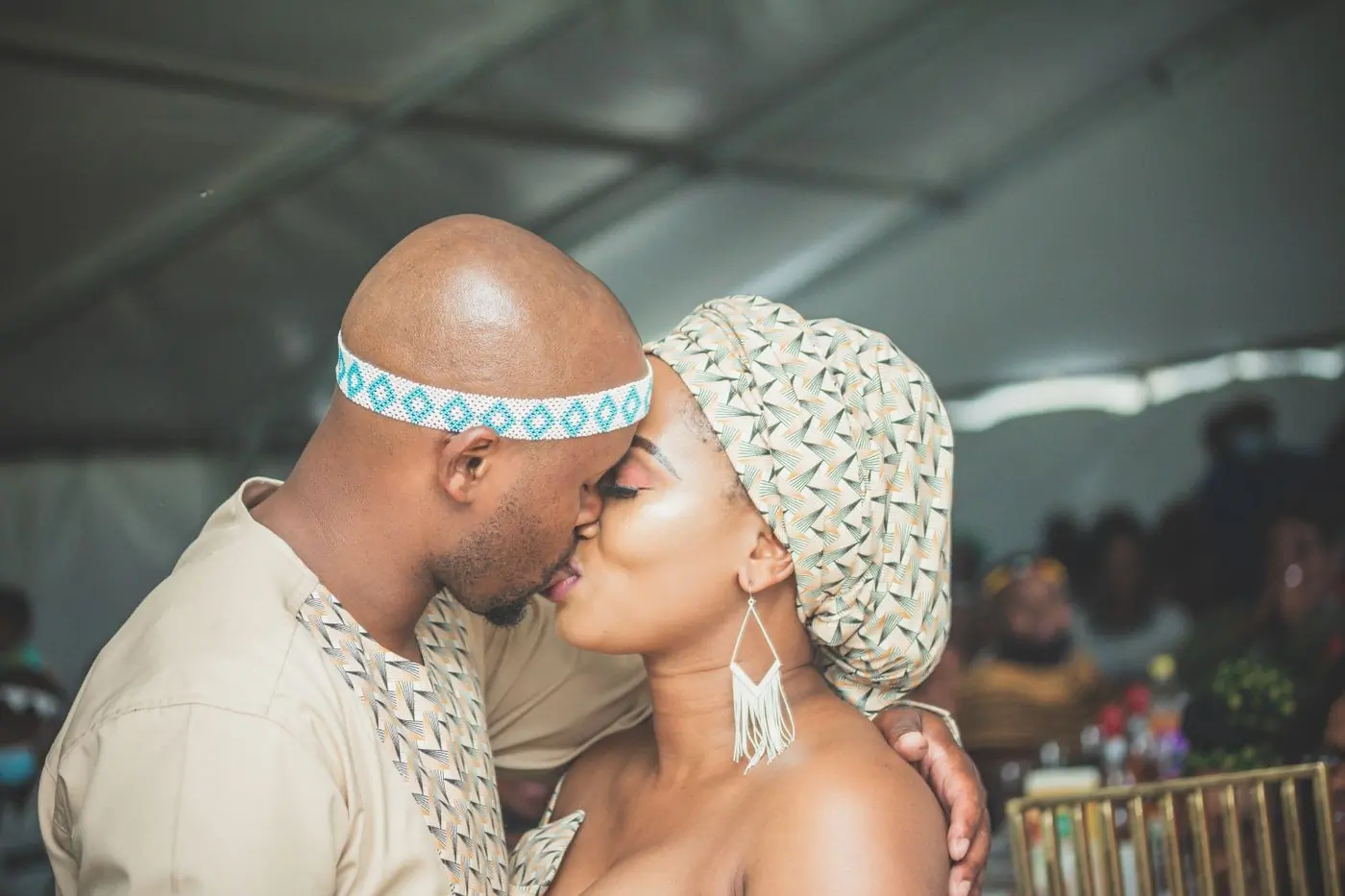 A couple in traditional cloth and beads sharing a kiss at their engagement ceremony