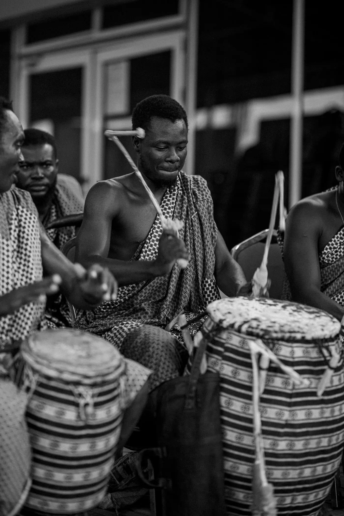 Drummers in traditional cloth playing at a ceremony, in black and white