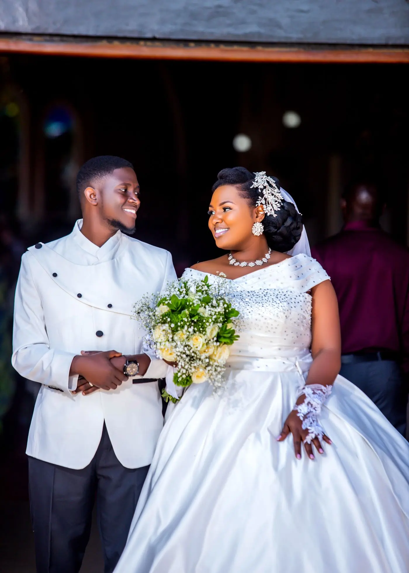 A bride and groom in white looking at each other during the vows, the bride holding a bouquet