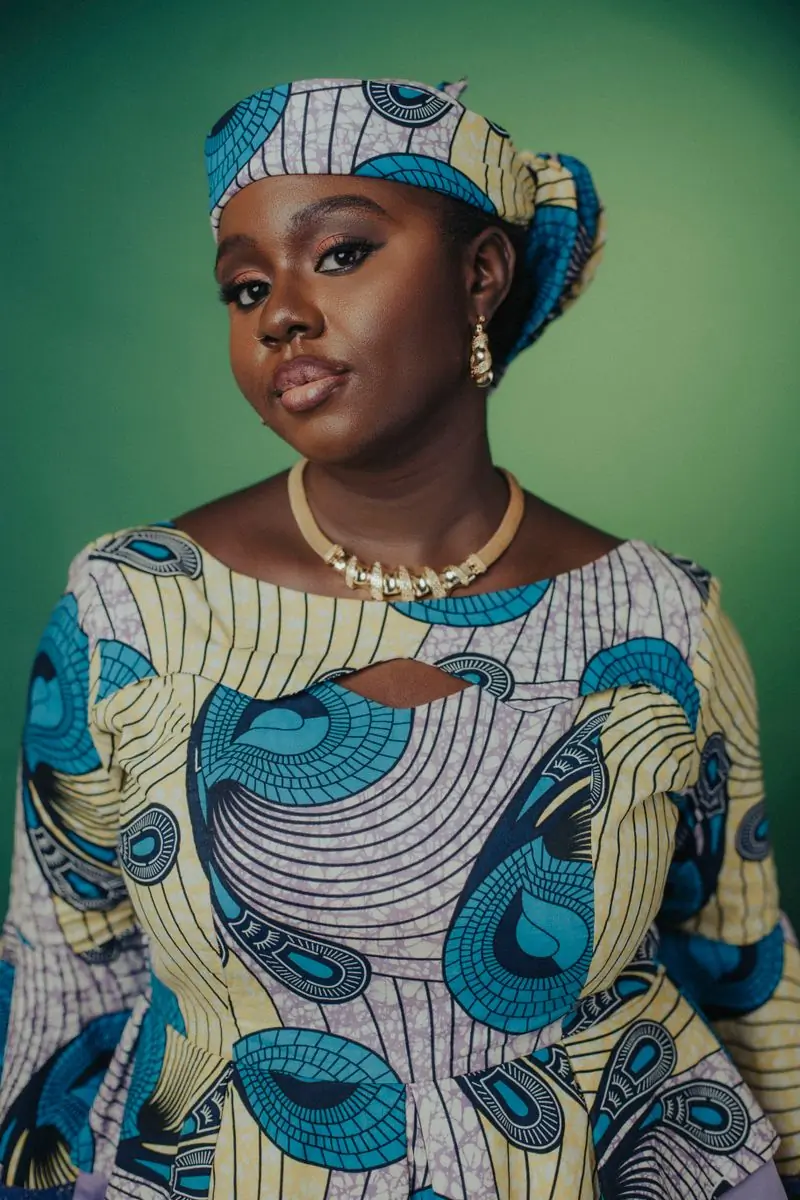 A woman in patterned cloth against a green backdrop