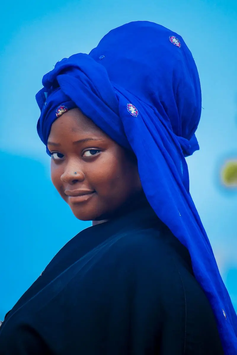 A woman in a blue headwrap against a bright backdrop