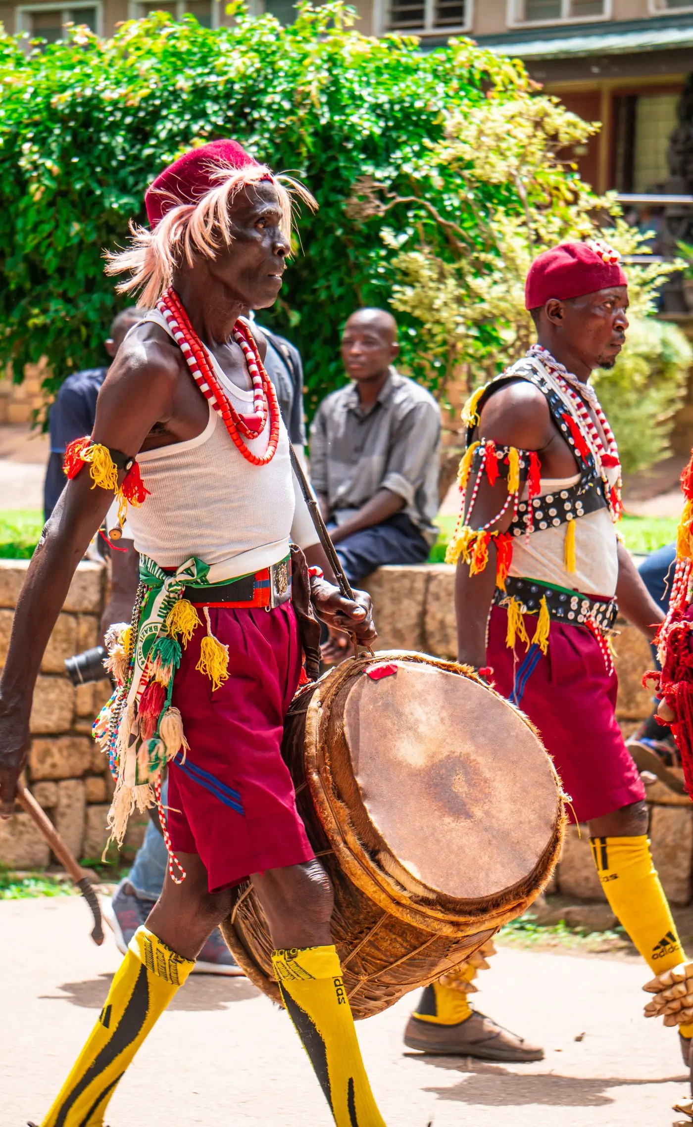 Drummers in beaded costume carrying their drums through a street procession