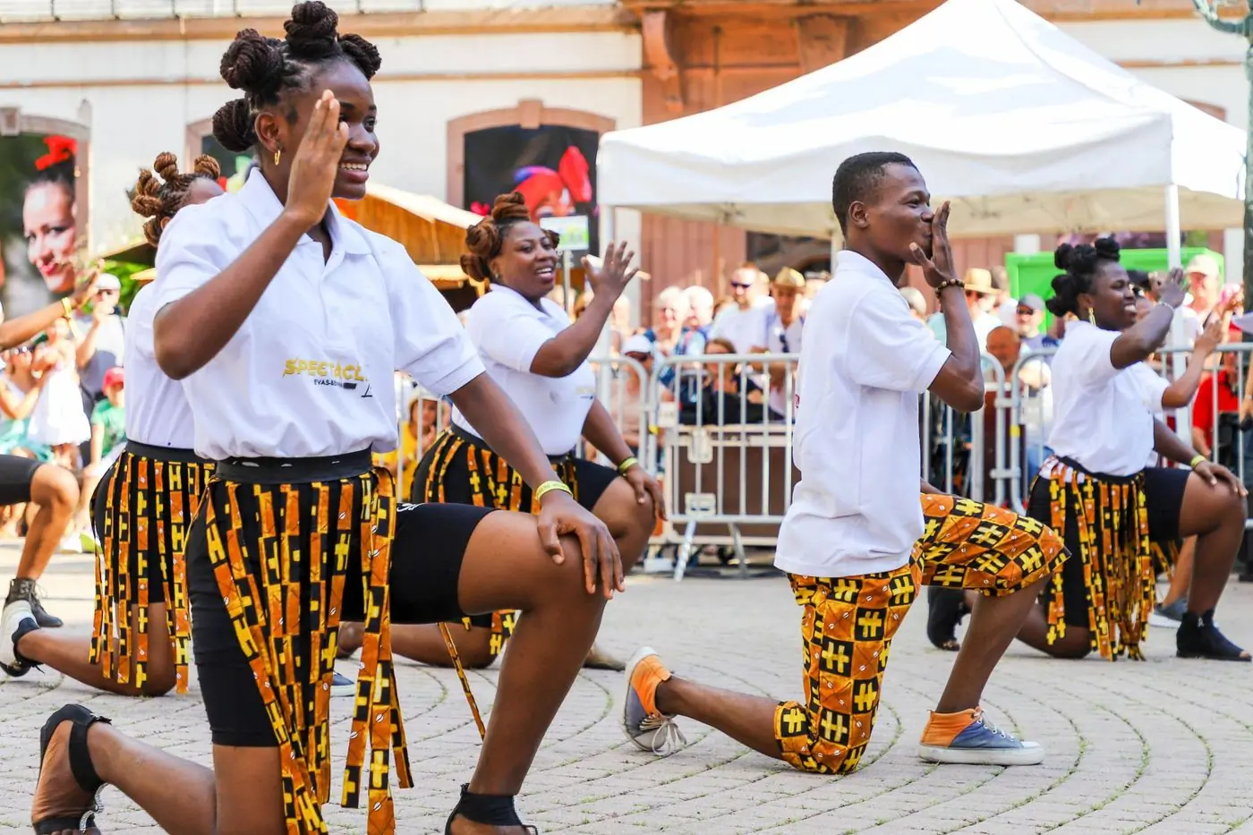 Dancers in kente kneeling mid-routine at a street festival
