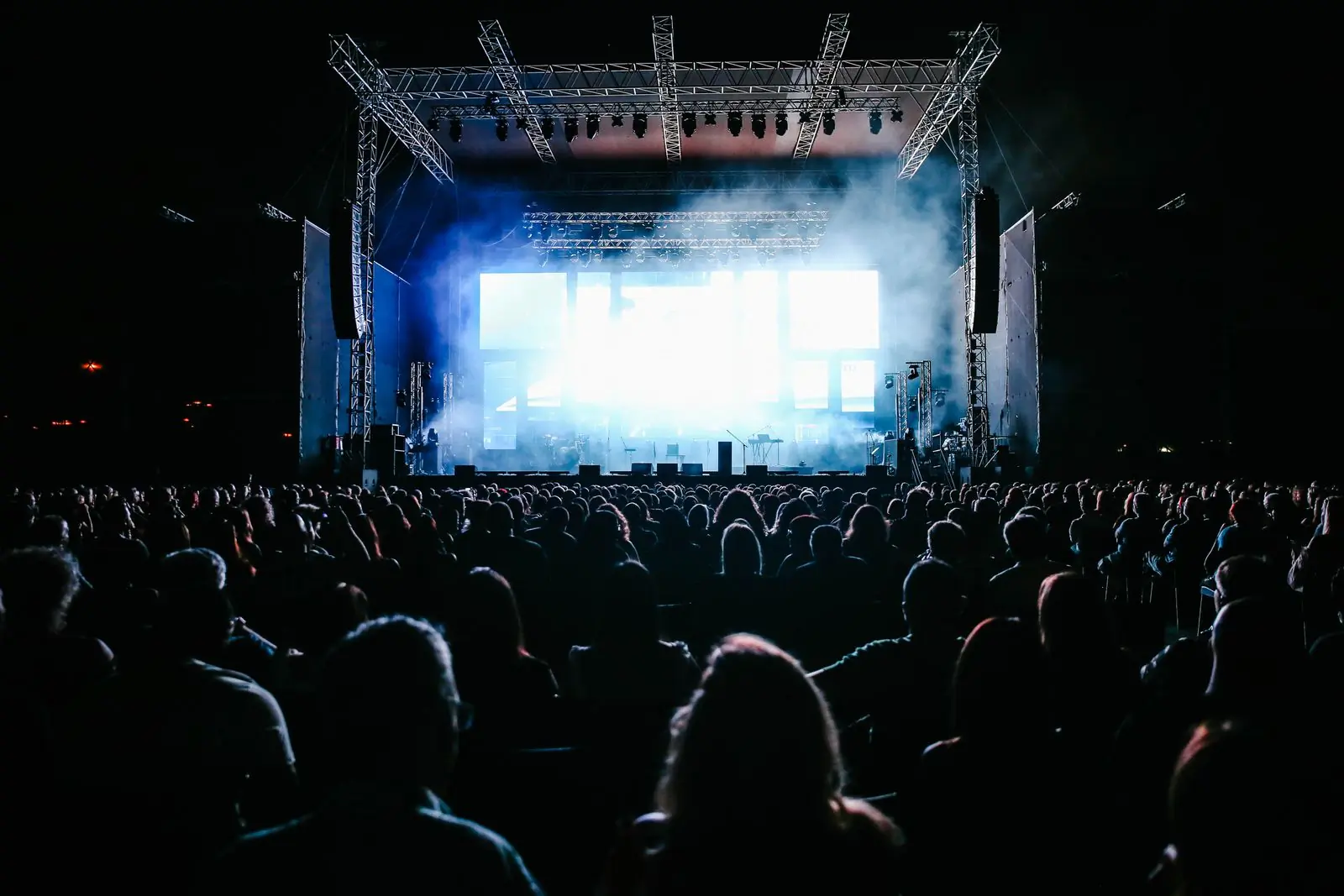 A festival crowd in silhouette against the lit main stage at night