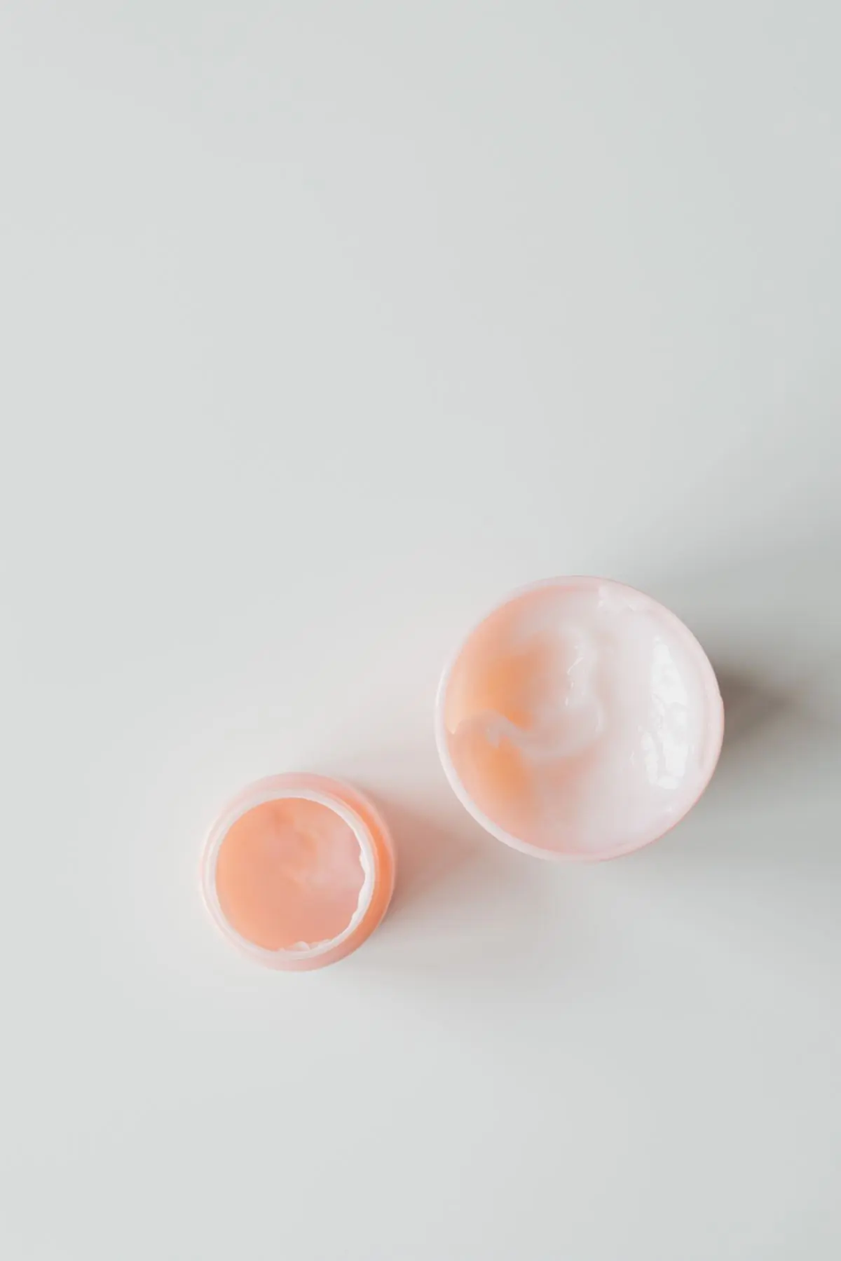 Two open pots of swirled apricot and white cream photographed from above on a pale grey surface