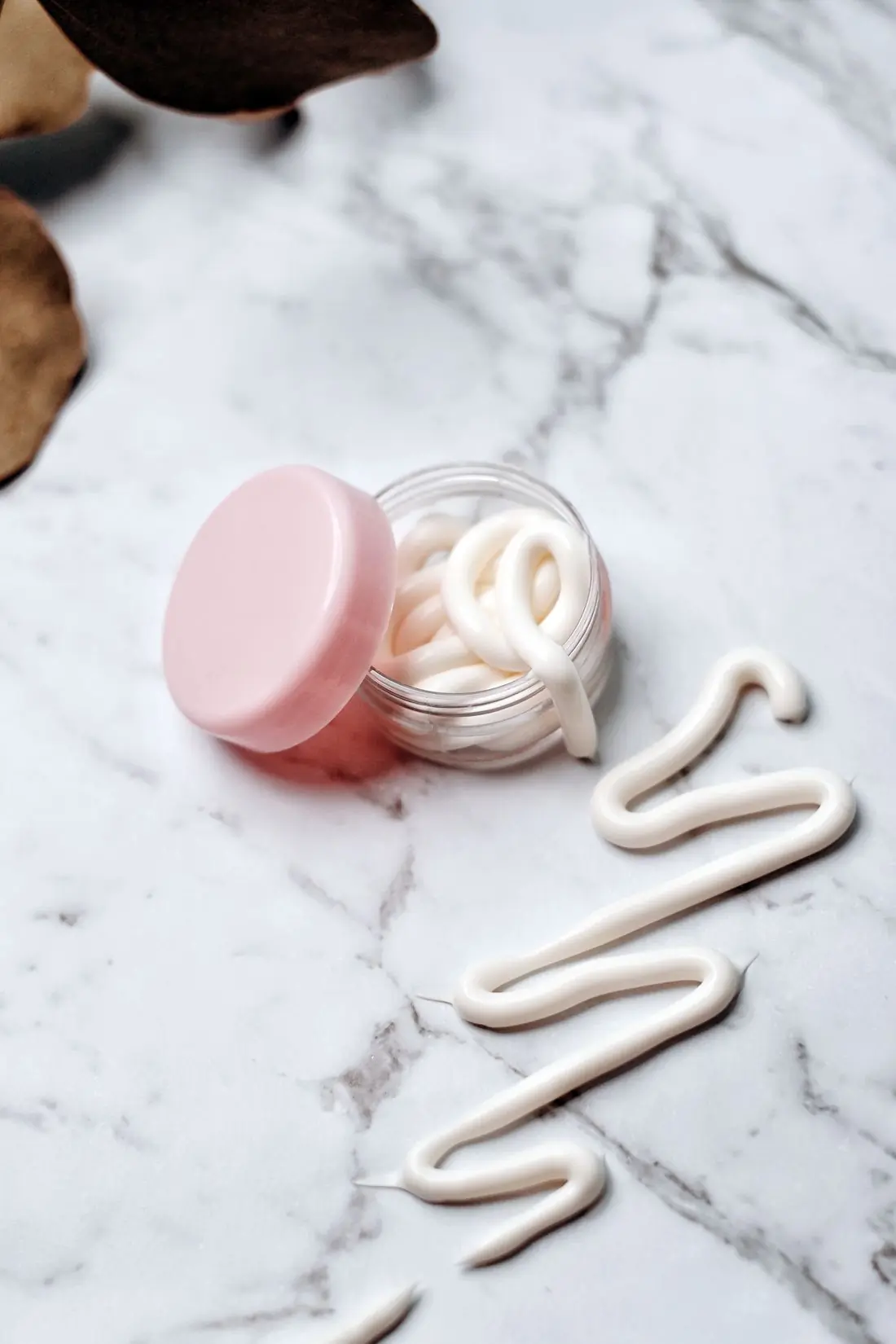 An open glass jar with a pink lid on white marble, cream piped beside it in loose squiggles