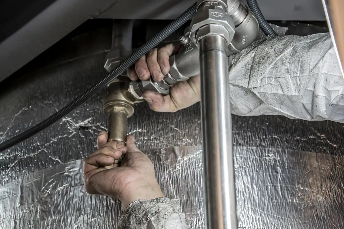 A plumber making up chrome pipework under a fitted unit