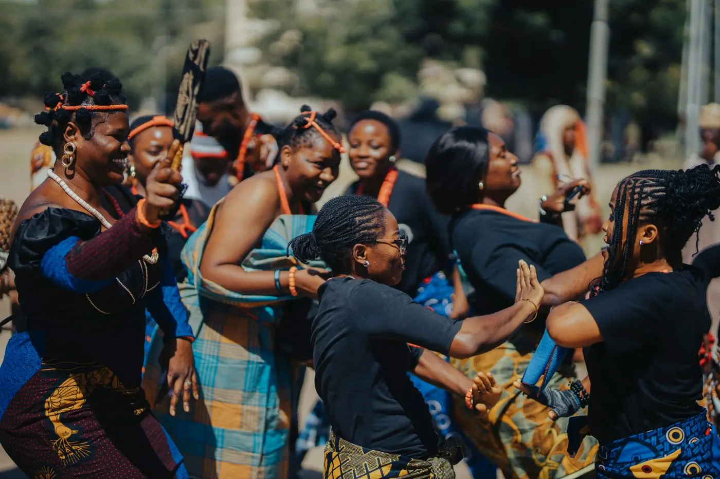 Women in bright wax-print dresses dancing together at a street festival