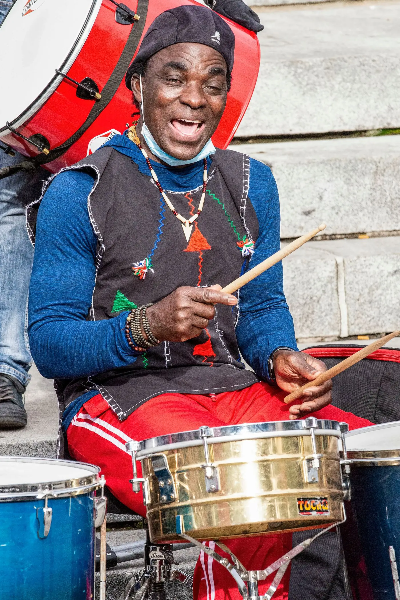 A drummer in a bright blue and red shirt playing a set of drums outdoors