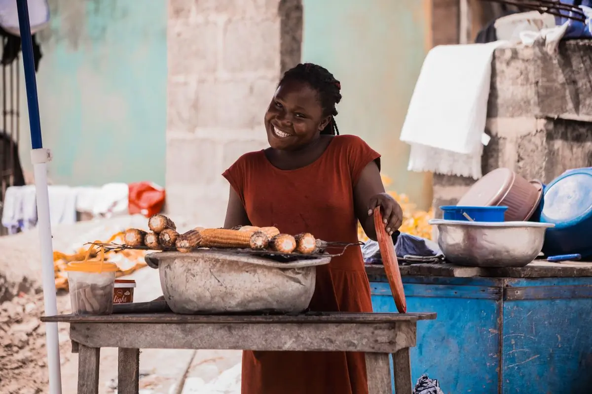 A street vendor smiling beside a grill of roasted corn