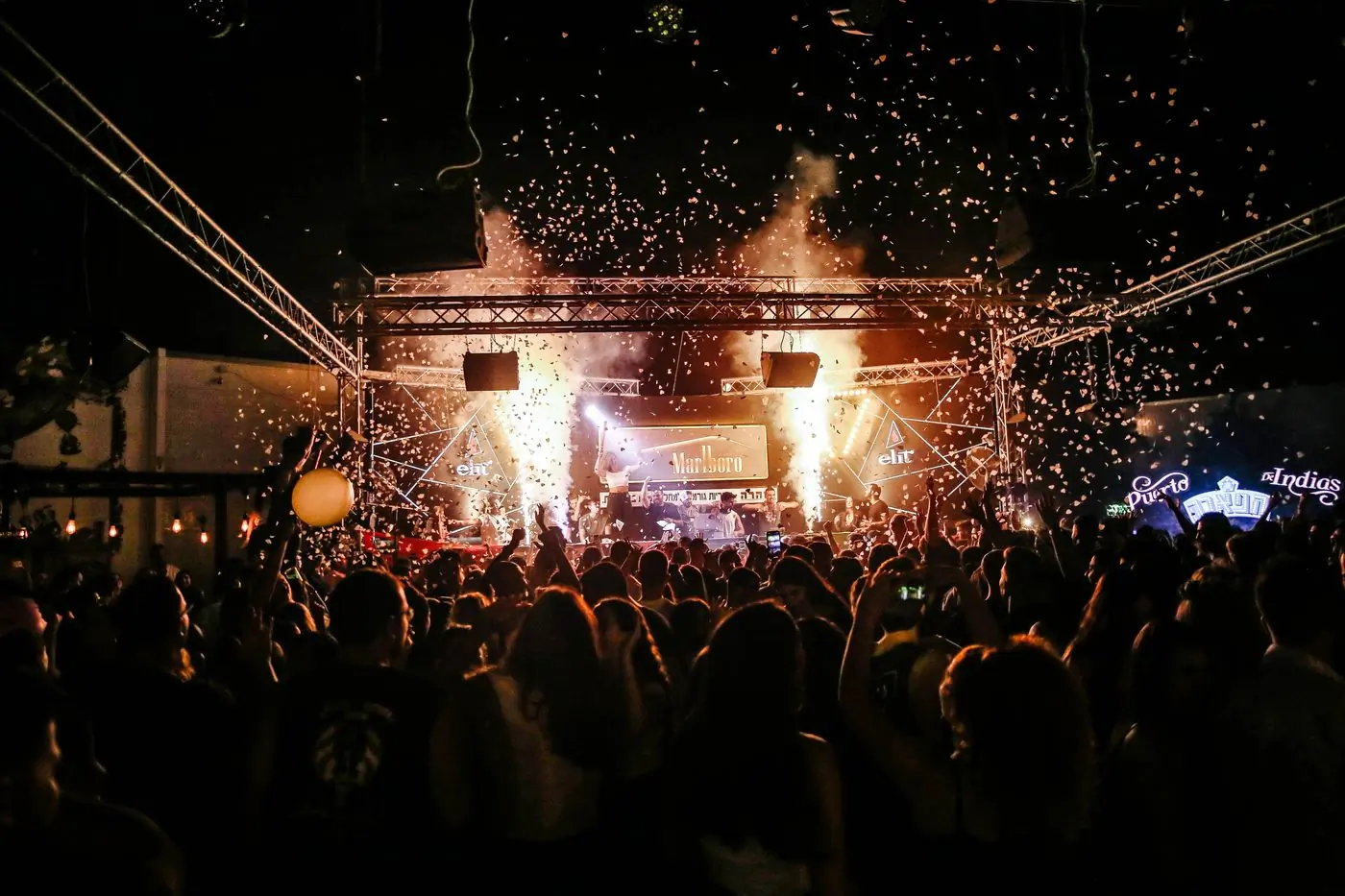 A festival crowd in front of a stage lit warm at night
