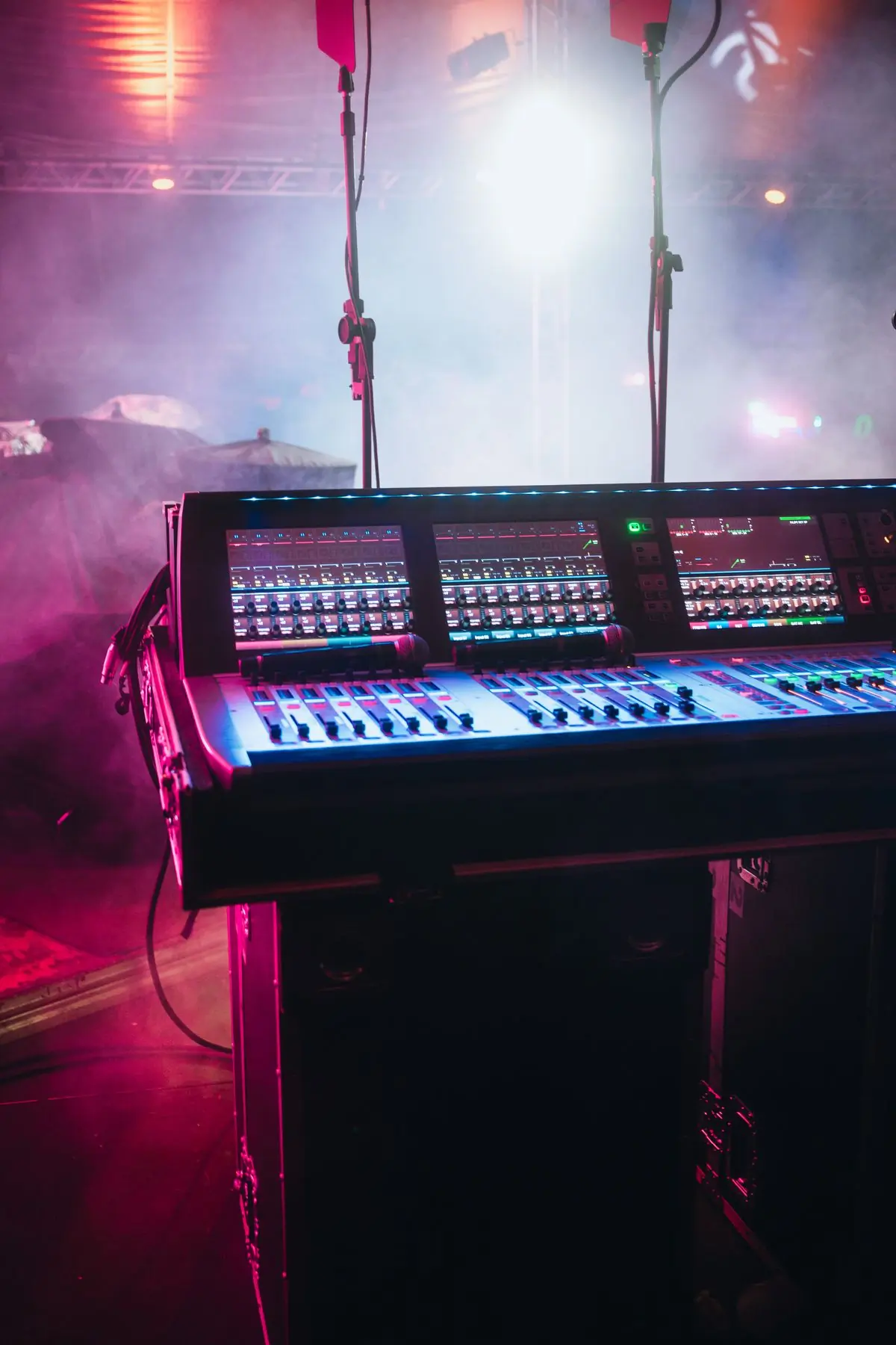 A front-of-house mixing desk under coloured stage lighting