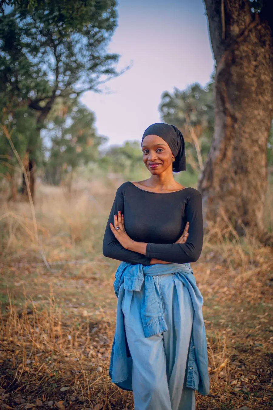 A woman with folded arms standing in open country at golden hour