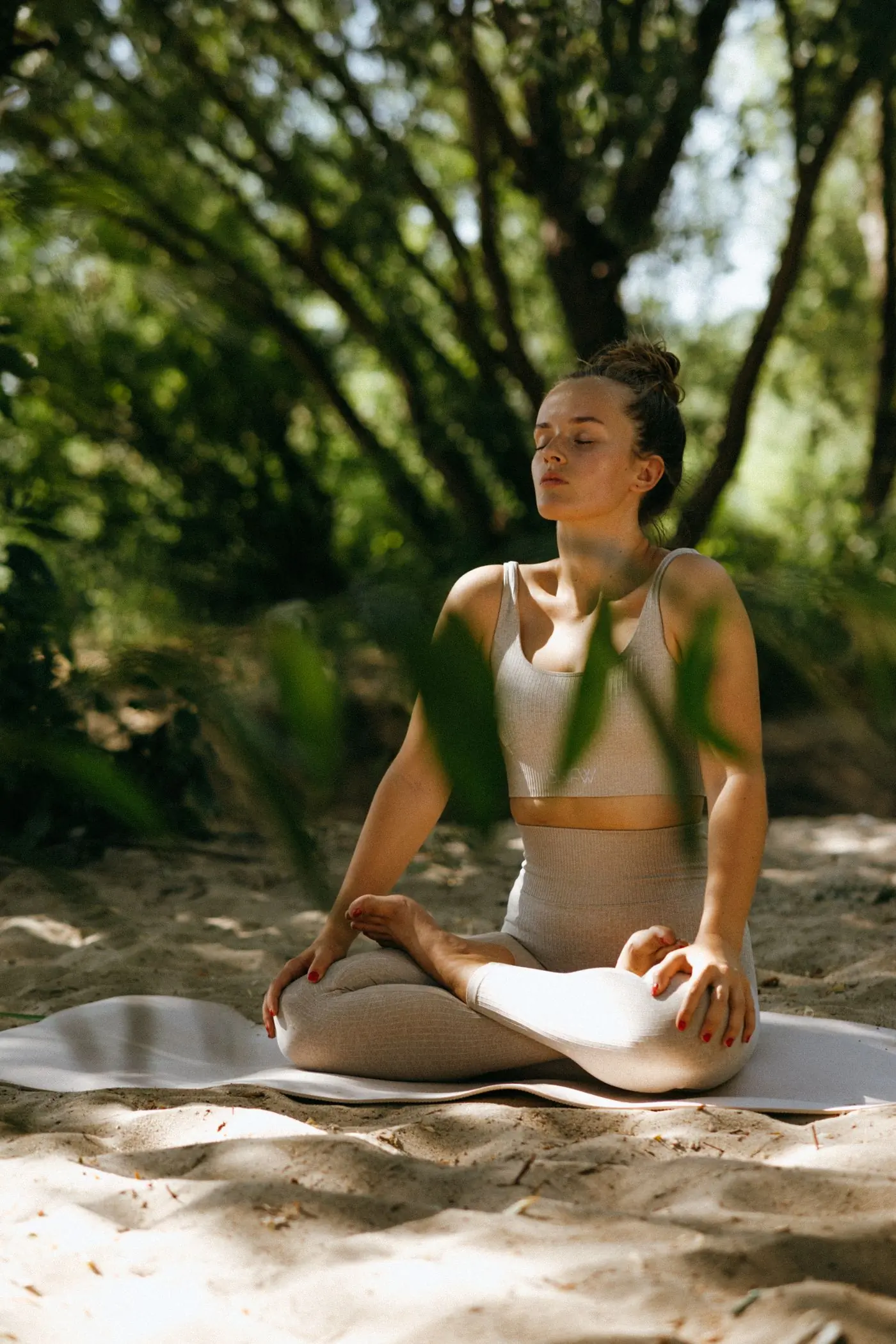 A woman sitting in meditation in dappled forest light
