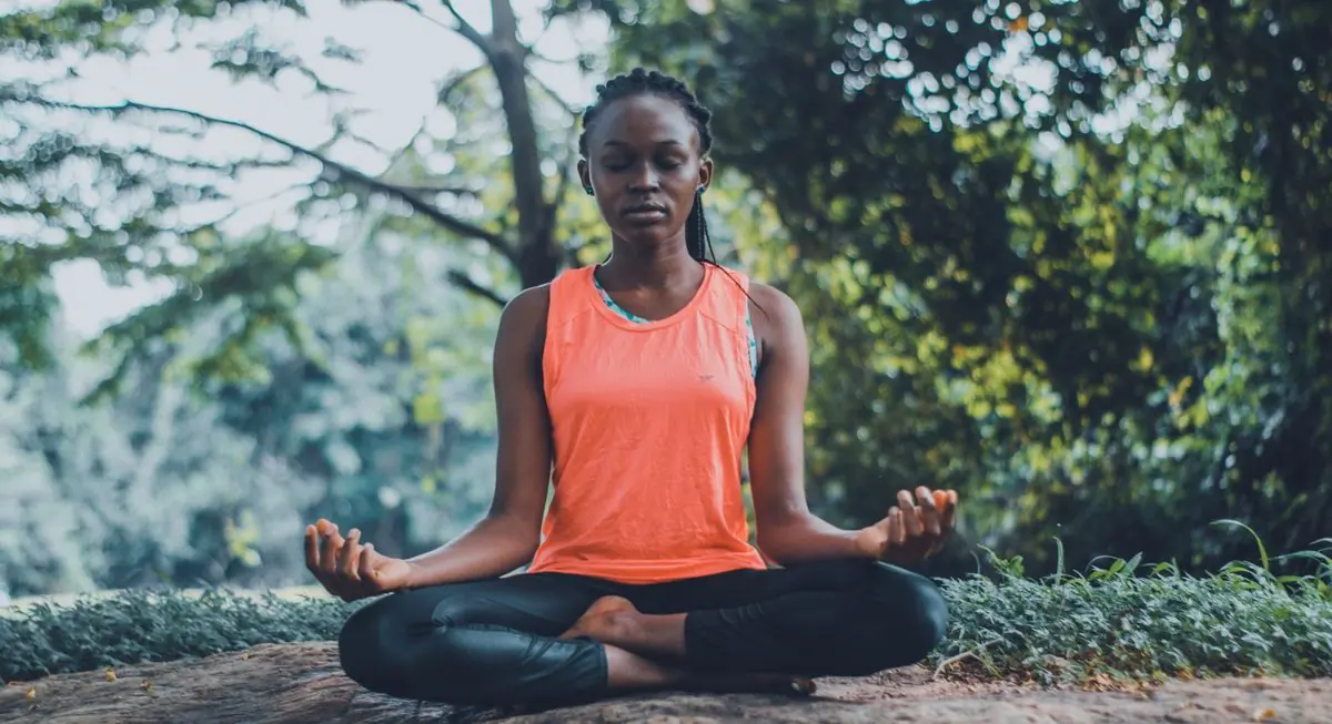 A woman sitting cross-legged in meditation among tall green plants