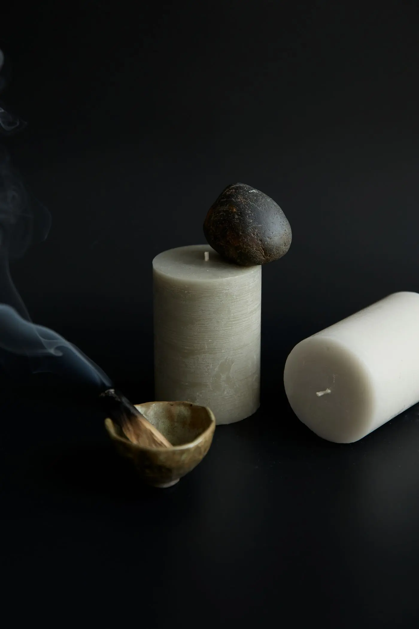 Candles and burning incense arranged with stones against a dark ground