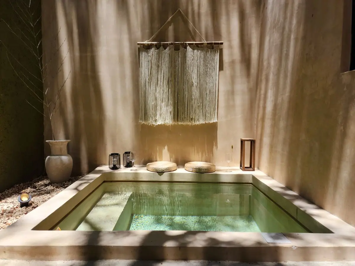 A sunlit stone plunge bath under a woven wall hanging
