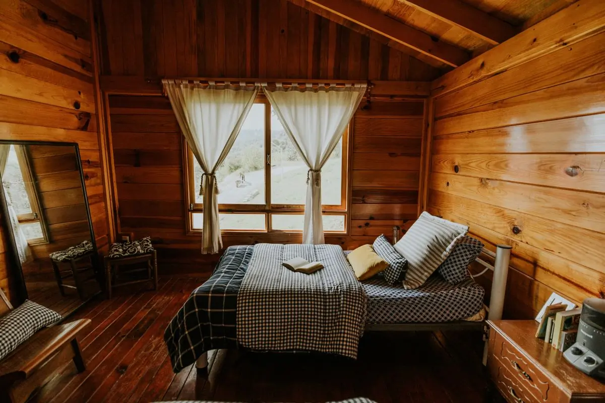 A warm wooden bedroom under a pitched roof with curtained windows