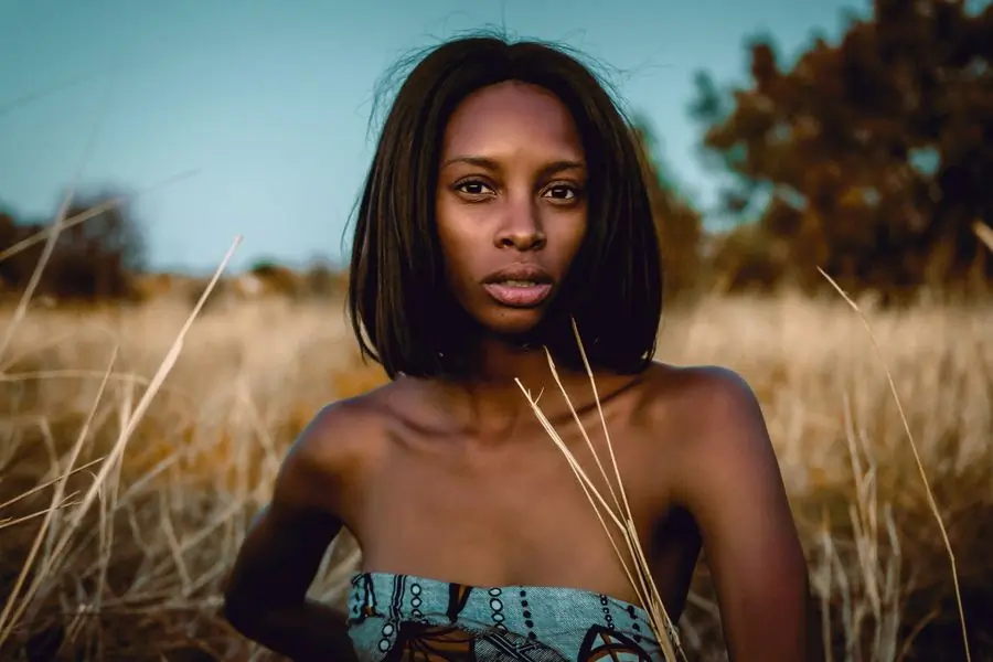 A woman standing in tall grass at dusk, looking towards the camera