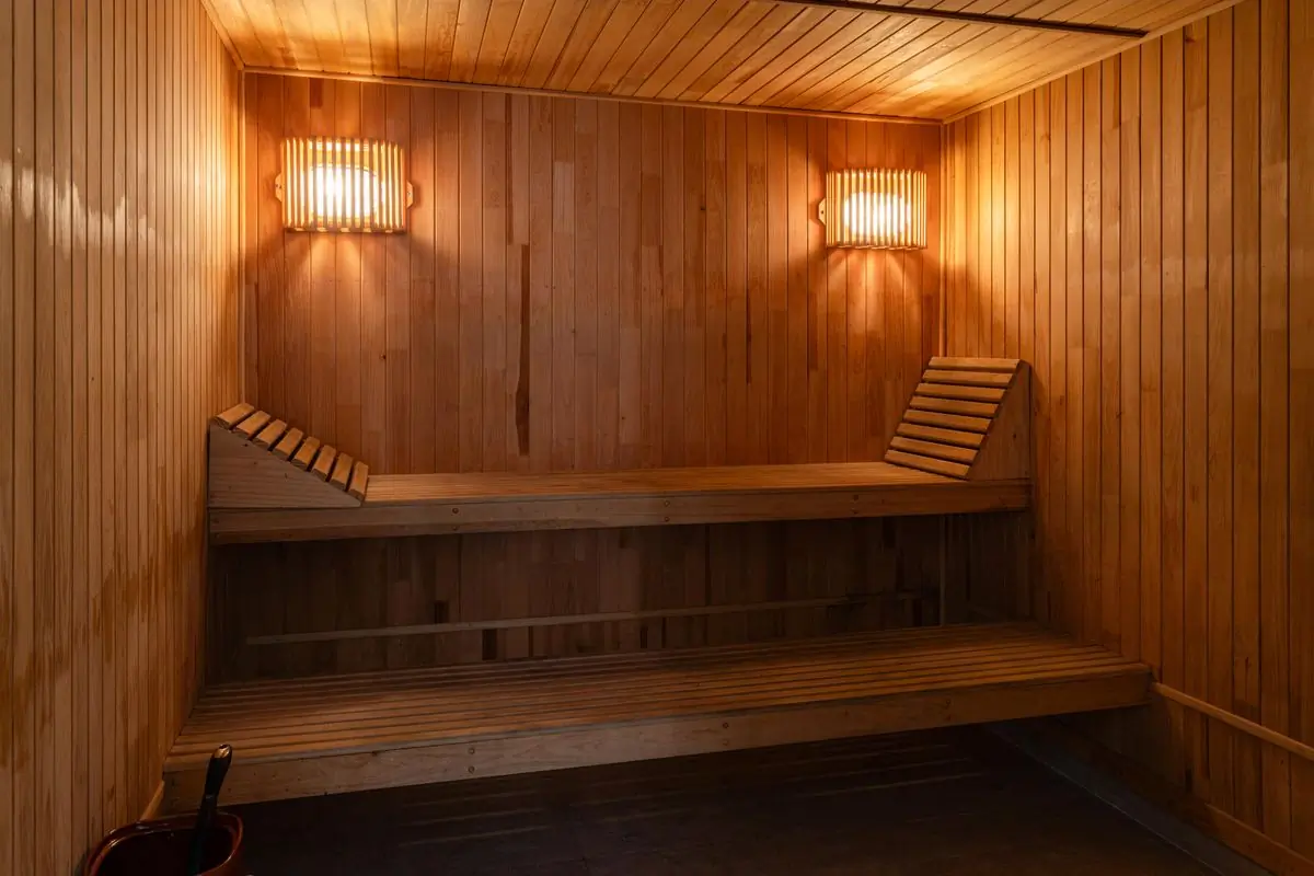 The timber interior of a cedar sauna lit by two warm wall lamps