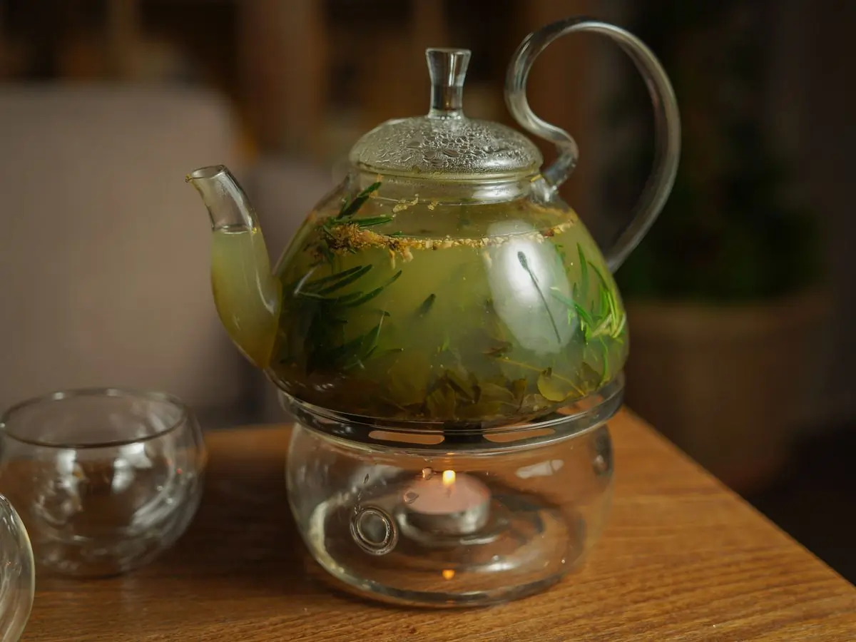 A glass teapot of herbal infusion warming over a candle flame