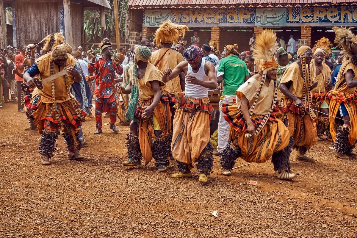 Masked dancers in raffia moving through a village square
