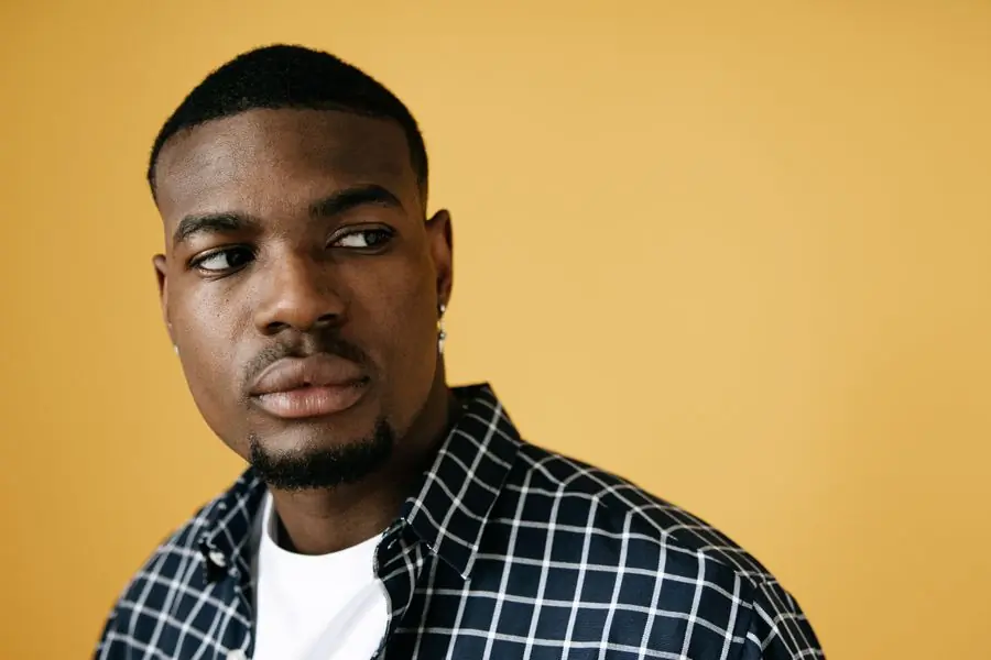 A rapper in a check shirt against a yellow backdrop