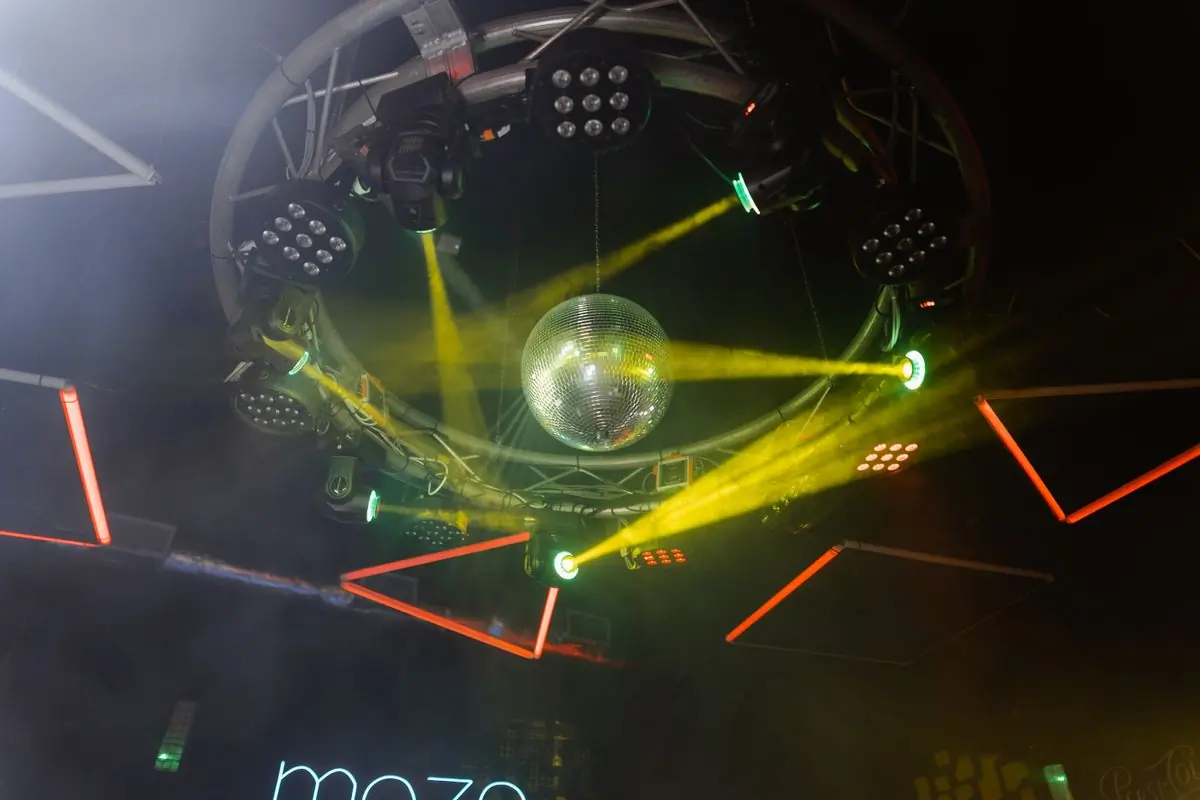 A mirror ball and coloured beams across a dark ceiling