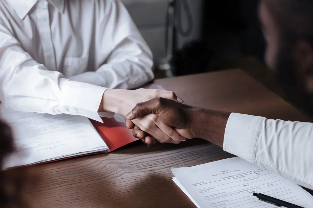 Two people shaking hands over a signed agreement