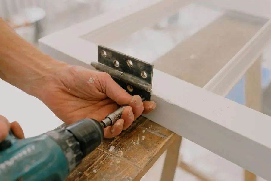 A workman drilling a hinge onto a window frame