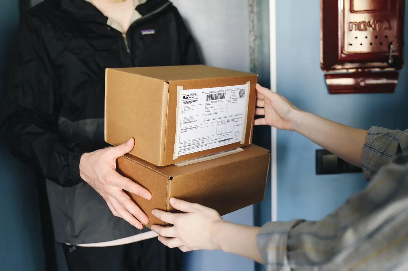 Two kraft boxes changing hands at a blue doorway