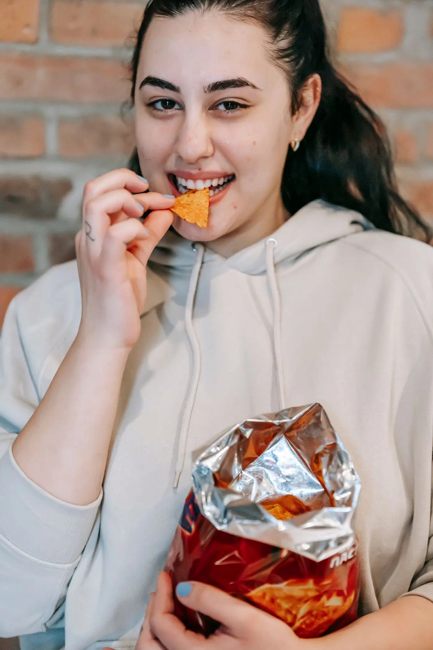 A woman mid-bite against a brick wall, bag in hand