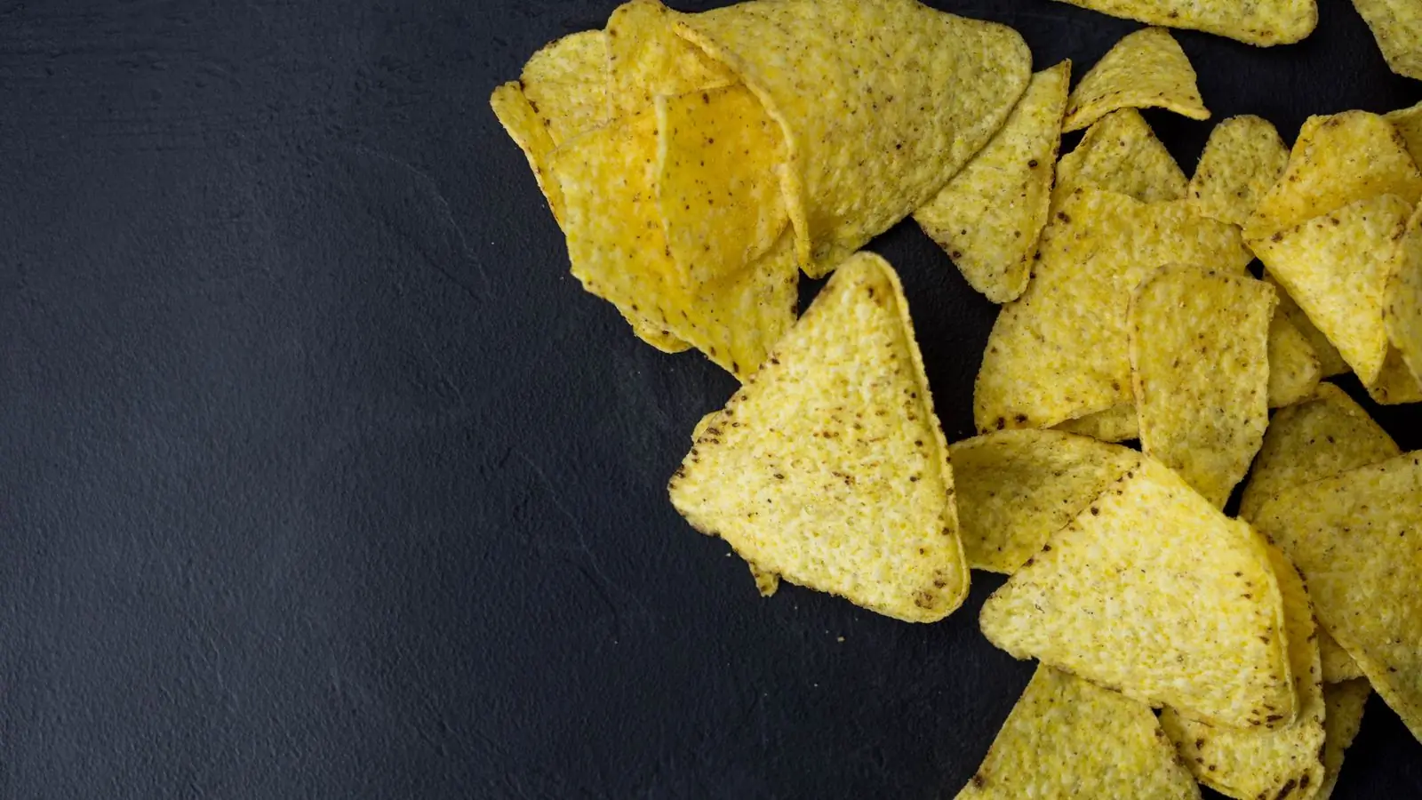 Tortilla chips spilling across a near-black slate counter, lit hard from the side