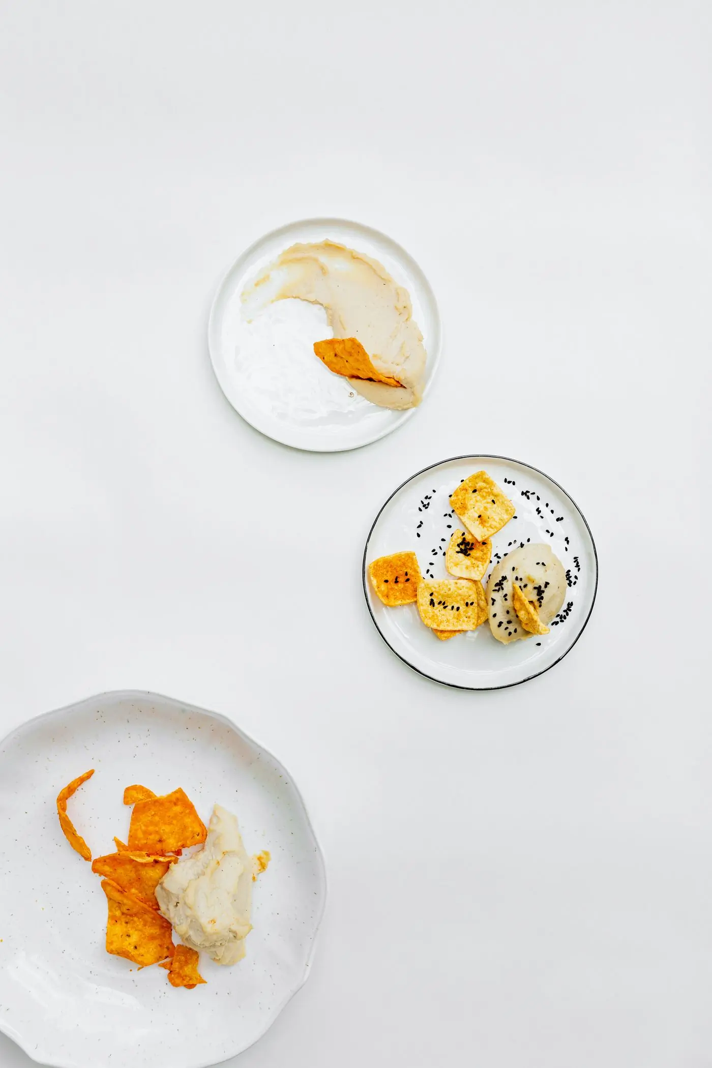 Three plates of chips and dips laid out on white