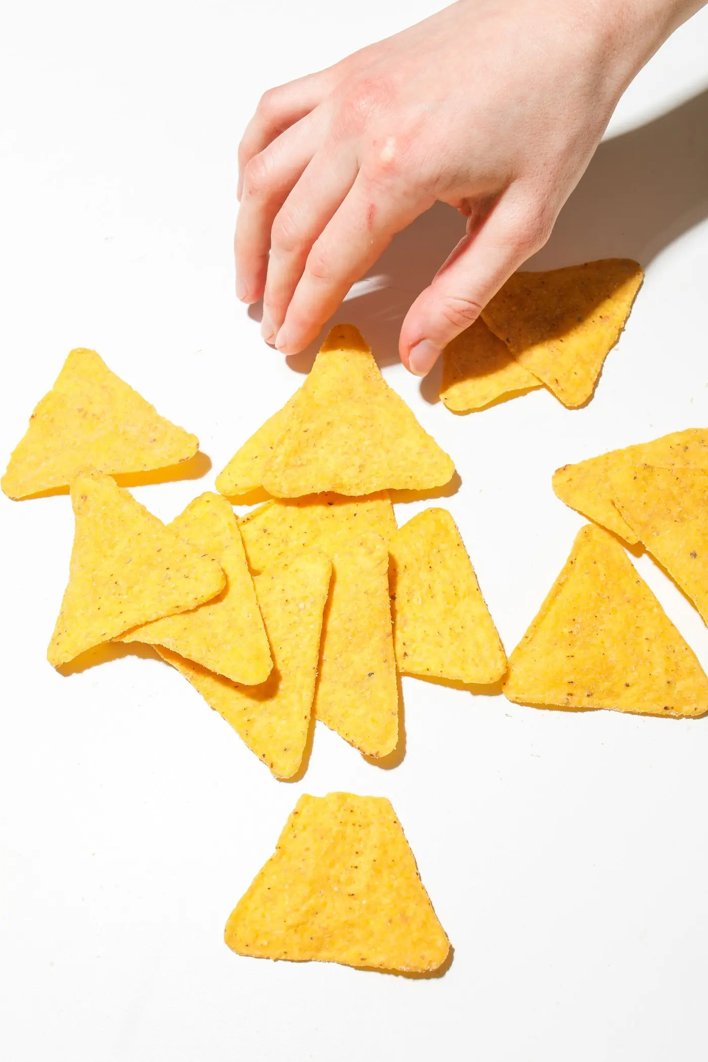 A hand reaching into scattered nacho triangles on a white table