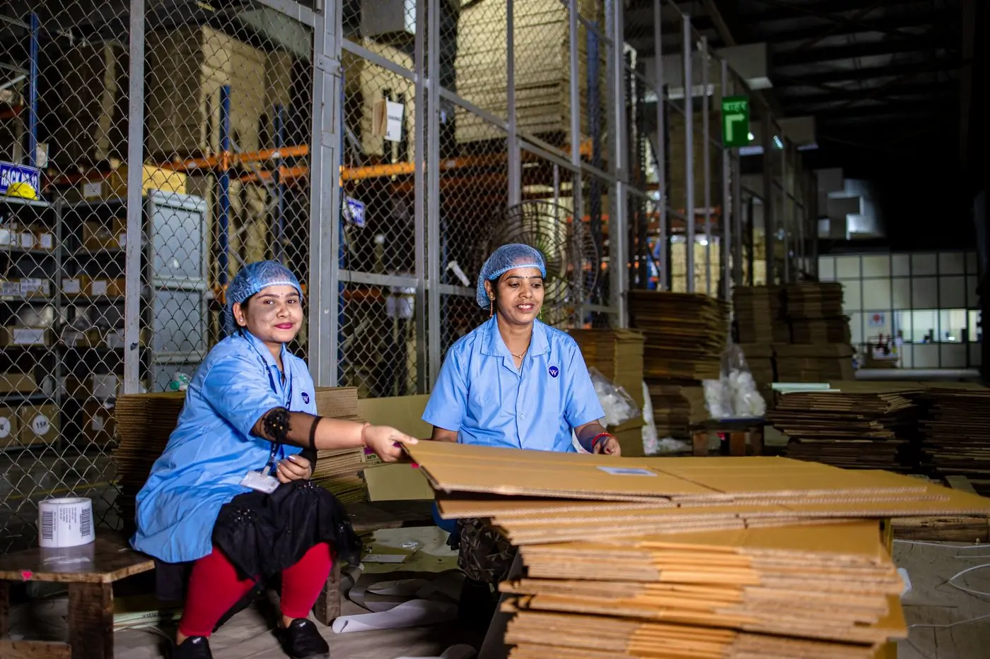 Two smiling women in blue uniforms and hairnets handling a cardboard box